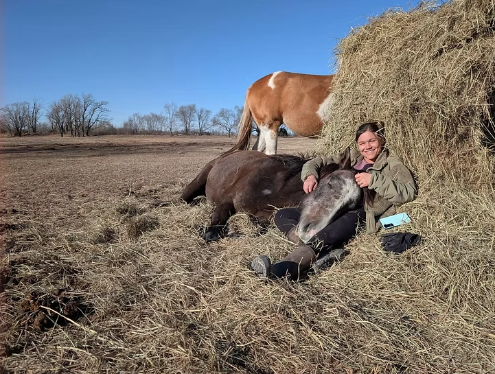 Vanessa sitting with her horses in a hay barn